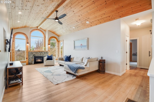 living area with wood finished floors, a stone fireplace, wooden ceiling, and a ceiling fan