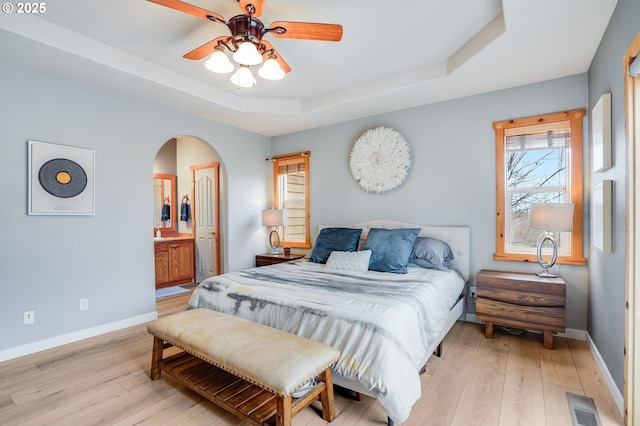 bedroom with a tray ceiling, arched walkways, visible vents, and light wood finished floors