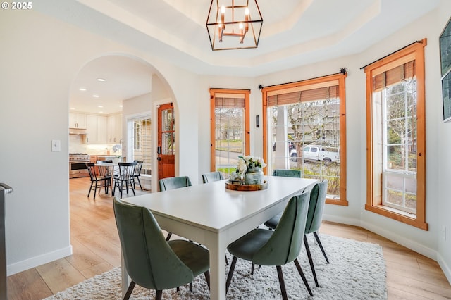 dining room with baseboards, light wood-type flooring, arched walkways, and a healthy amount of sunlight