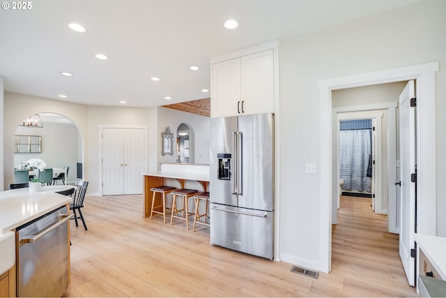 kitchen with light wood-type flooring, recessed lighting, arched walkways, and stainless steel appliances