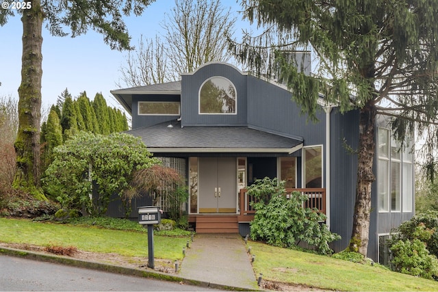 view of front of house featuring a shingled roof, a front yard, and covered porch