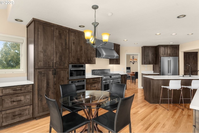 kitchen featuring high end appliances, light countertops, hanging light fixtures, an inviting chandelier, and wall chimney exhaust hood