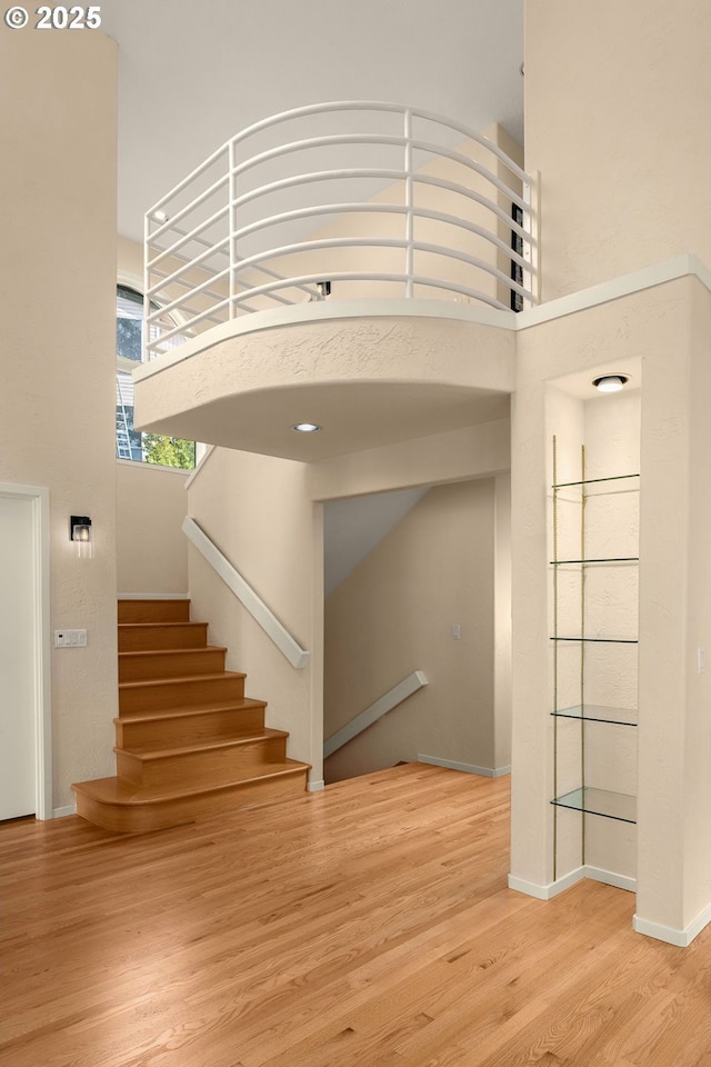 staircase featuring a towering ceiling, baseboards, and wood finished floors