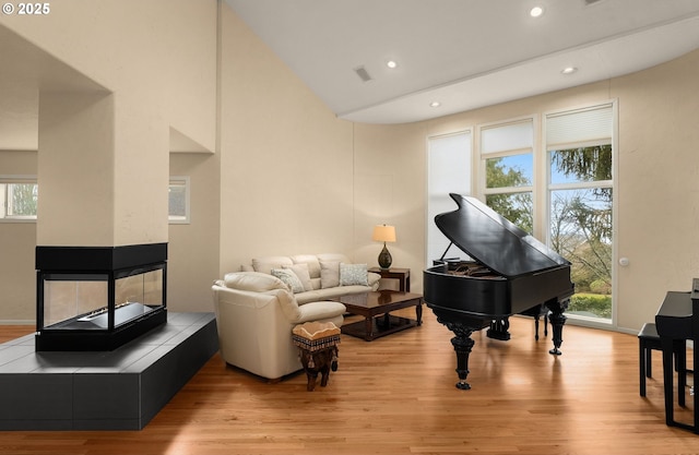 living area with lofted ceiling, recessed lighting, a fireplace, visible vents, and light wood finished floors