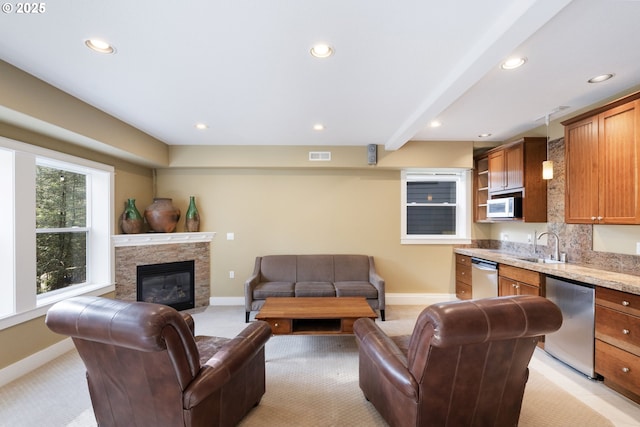 living room with sink, a stone fireplace, light colored carpet, and beamed ceiling