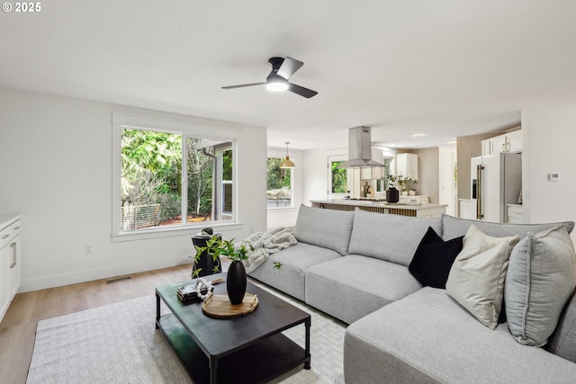 living room featuring a ceiling fan, baseboards, visible vents, and light wood finished floors