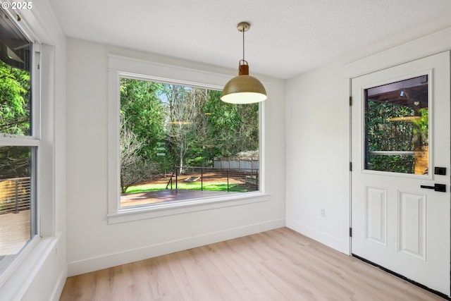 unfurnished dining area with a textured ceiling, baseboards, and wood finished floors