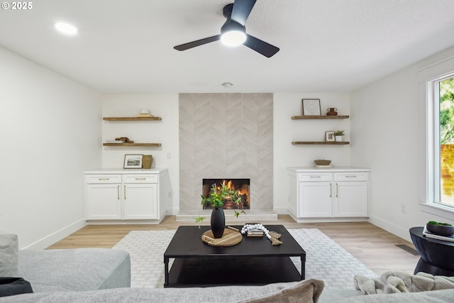 living room featuring light wood-type flooring, baseboards, a large fireplace, and ceiling fan