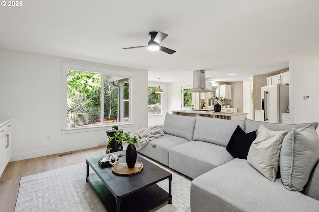 living area featuring light wood-style floors, ceiling fan, baseboards, and visible vents