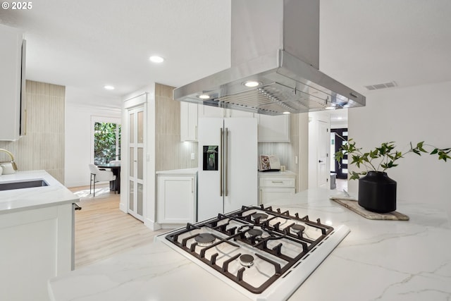 kitchen featuring white appliances, island exhaust hood, white cabinetry, and a sink