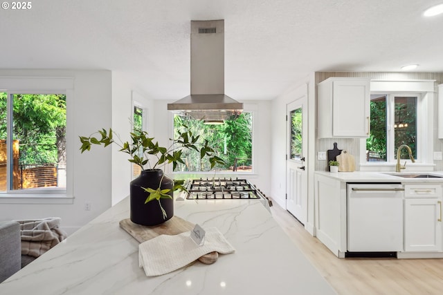 kitchen featuring white cabinets, stainless steel gas stovetop, dishwasher, island range hood, and a sink