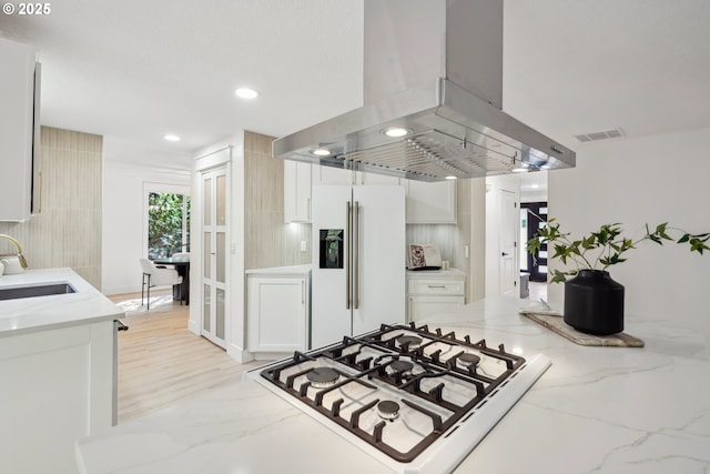 kitchen with island exhaust hood, white cabinets, a sink, and white appliances