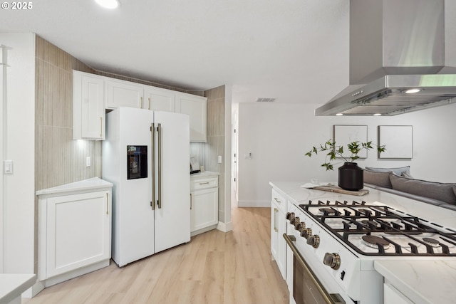 kitchen featuring white cabinets, white refrigerator with ice dispenser, wall chimney exhaust hood, and visible vents