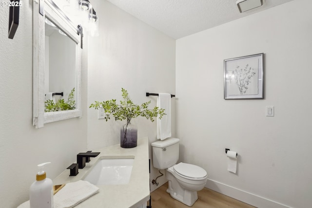 bathroom with vanity, a textured ceiling, toilet, visible vents, and wood finished floors