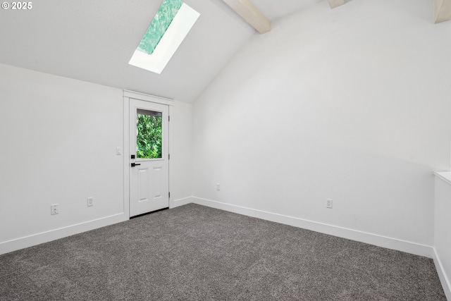 empty room with dark colored carpet, vaulted ceiling with skylight, and baseboards