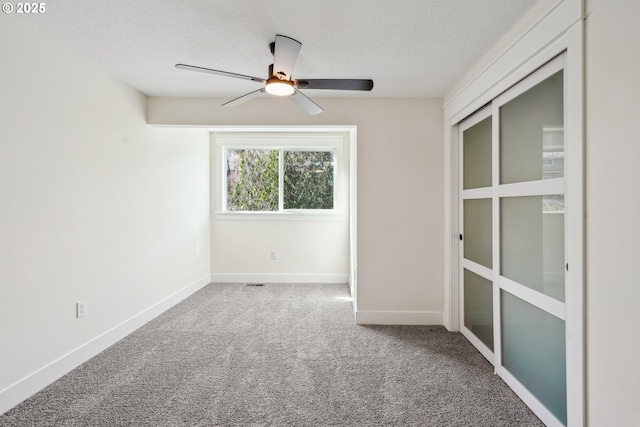 carpeted spare room featuring a textured ceiling, ceiling fan, and baseboards