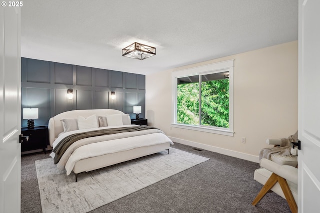 carpeted bedroom with visible vents, a decorative wall, a textured ceiling, and baseboards