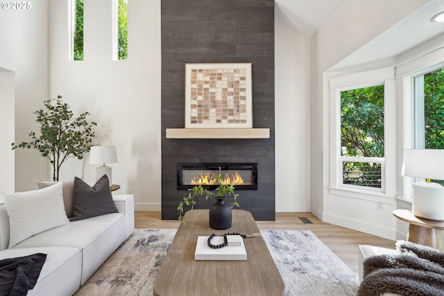 living room featuring a large fireplace, visible vents, baseboards, and wood finished floors