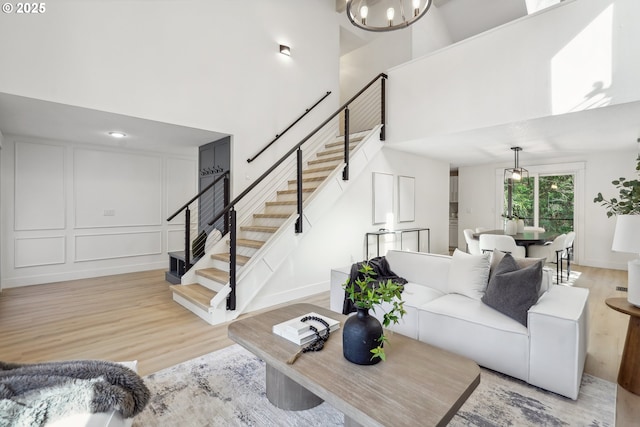 living room with a towering ceiling, light wood finished floors, stairway, and a decorative wall