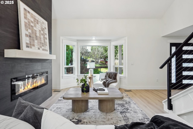 living room featuring stairway, baseboards, wood finished floors, and a tile fireplace