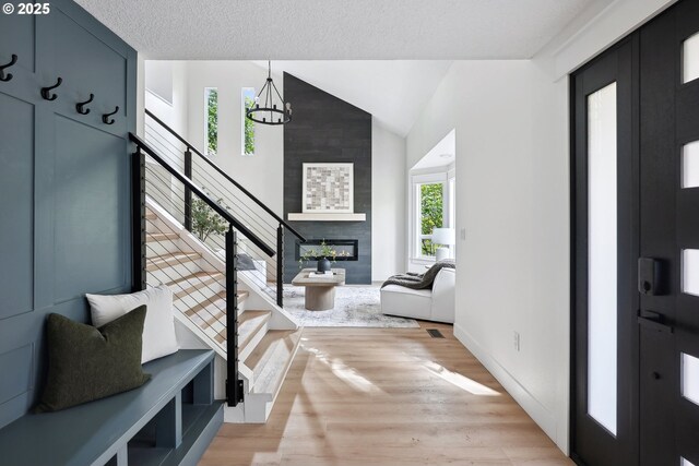 entrance foyer with light wood-type flooring, a chandelier, high vaulted ceiling, stairway, and a fireplace