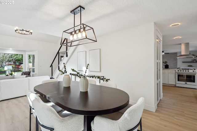 dining area featuring a textured ceiling, stairway, light wood-type flooring, and baseboards