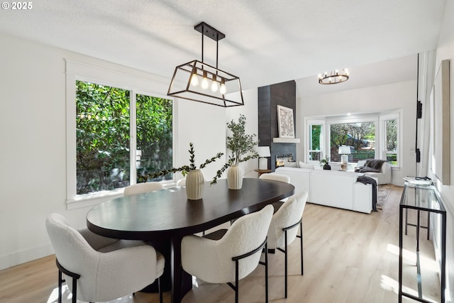 dining area featuring light wood-type flooring, an inviting chandelier, a fireplace, and a textured ceiling