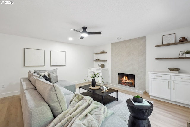 living room featuring light wood-type flooring, a tile fireplace, a ceiling fan, and baseboards