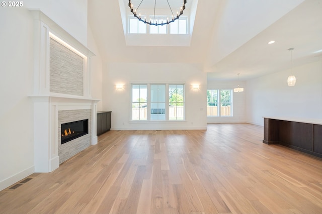unfurnished living room with light wood-style flooring, a glass covered fireplace, visible vents, a notable chandelier, and high vaulted ceiling