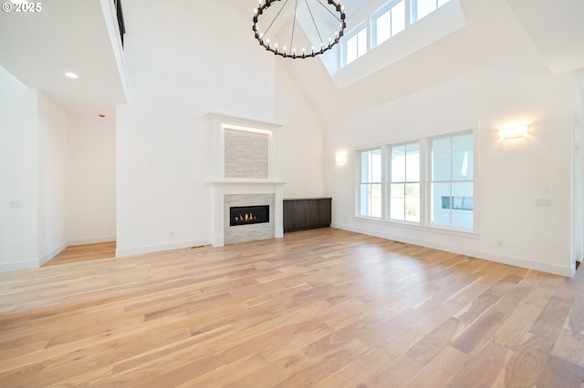 unfurnished living room featuring baseboards, a glass covered fireplace, light wood finished floors, a towering ceiling, and a notable chandelier
