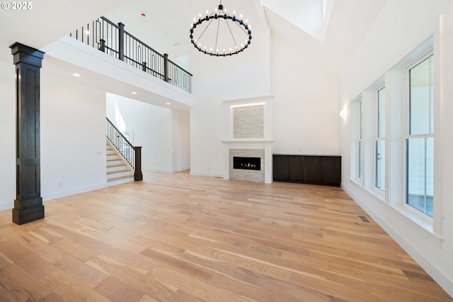 unfurnished living room with a warm lit fireplace, high vaulted ceiling, baseboards, and light wood-style floors