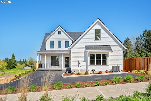 view of front of home with cooling unit, a shingled roof, covered porch, and fence