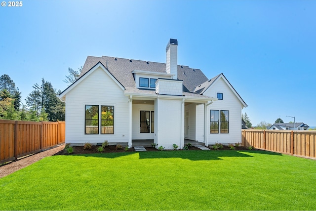 rear view of house featuring a lawn, a chimney, a shingled roof, and a fenced backyard