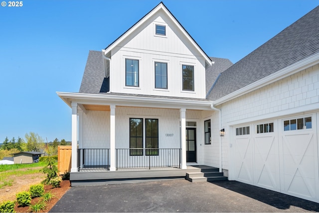 modern inspired farmhouse featuring covered porch, a garage, and a shingled roof