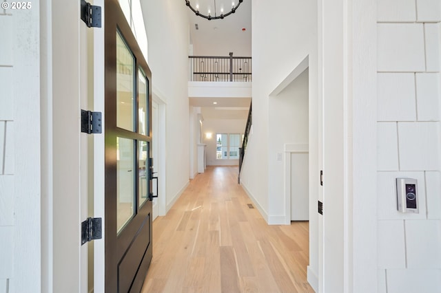 corridor featuring a high ceiling, baseboards, a chandelier, and light wood-style floors