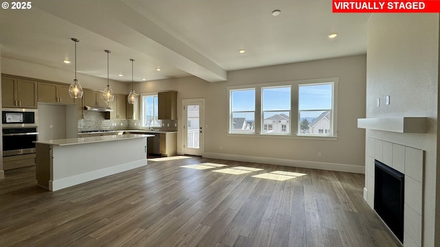 kitchen with under cabinet range hood, light countertops, dark wood-type flooring, tasteful backsplash, and appliances with stainless steel finishes