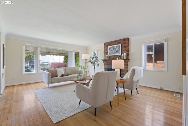 living room with a brick fireplace, baseboards, and light wood finished floors