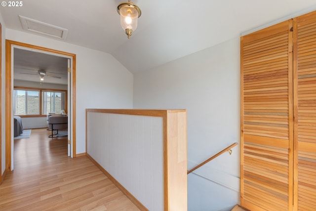 corridor featuring an upstairs landing, light wood-style floors, attic access, and lofted ceiling
