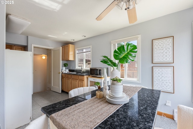 kitchen with stainless steel microwave, dark countertops, ceiling fan, baseboards, and freestanding refrigerator