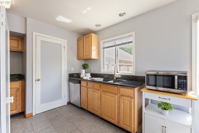 kitchen featuring stainless steel appliances, a sink, granite tiled floors, light brown cabinets, and baseboards