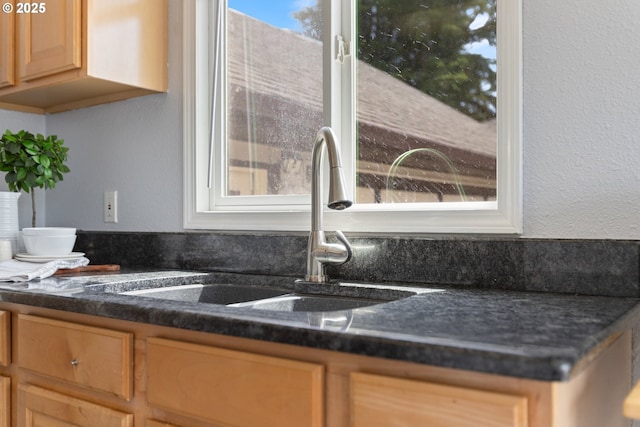 kitchen with a sink, light brown cabinetry, and dark countertops
