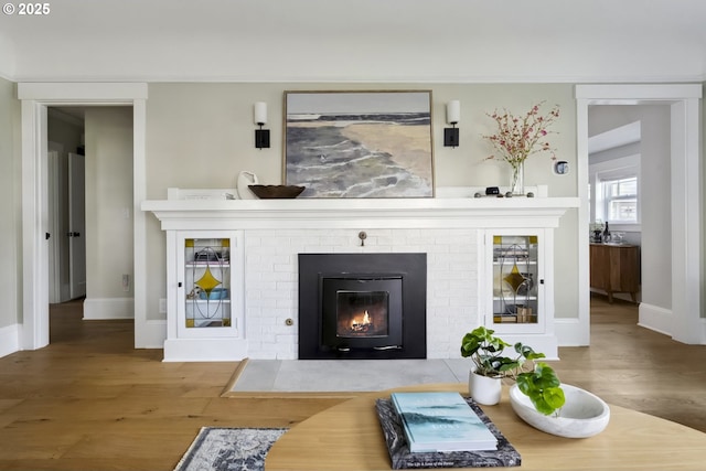 living room with a brick fireplace, baseboards, and wood finished floors