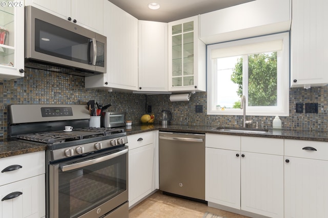 kitchen featuring stainless steel appliances, a sink, decorative backsplash, white cabinets, and glass insert cabinets