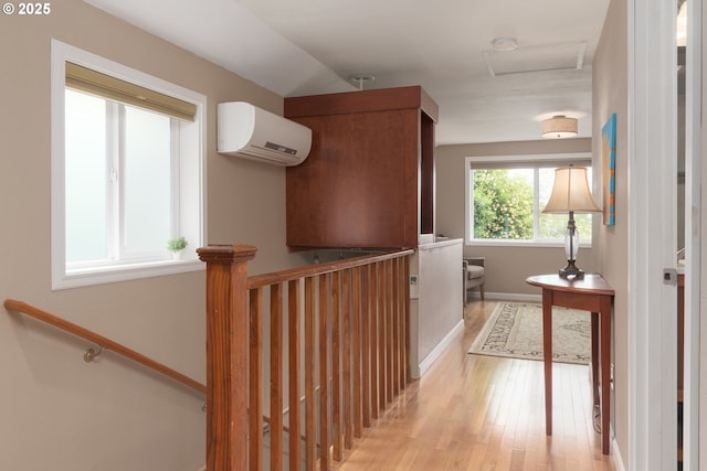 corridor with a wall mounted air conditioner, attic access, light wood-style flooring, baseboards, and an upstairs landing
