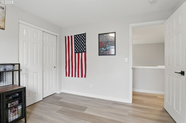 unfurnished bedroom featuring light wood finished floors, baseboards, and a closet