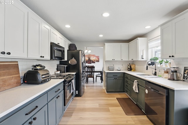 kitchen with black appliances, a sink, tasteful backsplash, light wood finished floors, and white cabinetry