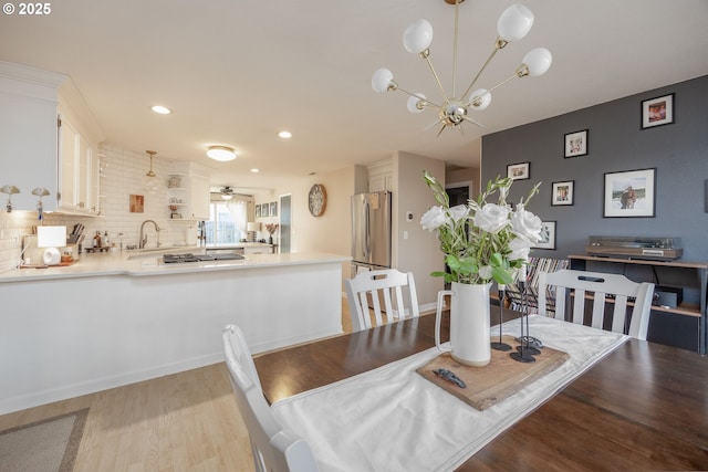 dining area with ceiling fan with notable chandelier, light hardwood / wood-style flooring, and sink