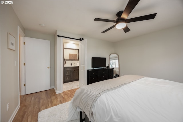 bedroom featuring light wood-type flooring, connected bathroom, a barn door, and ceiling fan