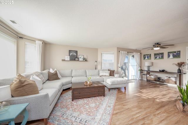 living room with ceiling fan, light wood-type flooring, and a textured ceiling