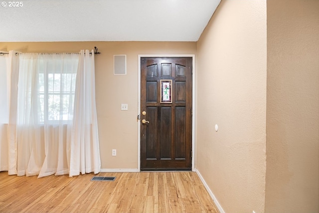 foyer entrance featuring light wood finished floors, visible vents, baseboards, and vaulted ceiling